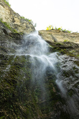 Waterfall hidden inside the forest, beauties of Slovenia to be discovered. Near Nova Gorica, Tolmin village. Water spray and vivid rainbow forms from the waterfall that falls sheer onto the rock.