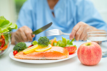 Asian elderly woman patient eating salmon steak breakfast with vegetable healthy food in hospital.