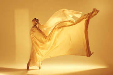 Dance of light. Artistic female ballet dancer in flowing golden dress making creative graceful...