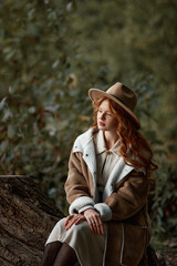 Red-haired girl in a hat and beige coat in the autumn forest. Graine effect used