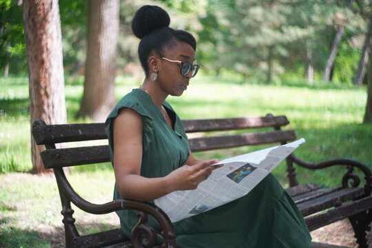 Beautiful and young black woman reading a newspaper in the park