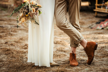 legs of a wedding couple close-up, the bride in a white dress holds a bouquet, the guy in brown boots, photo shoot of the newlyweds