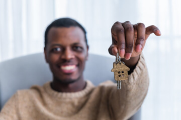 Joyful African American man holding up house keys, symbolizing new homeownership, with bright smile and casual sweater.