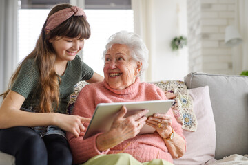 Grandmother with cute girl scrolling on tablet, girl teaching senior woman to work with technology,...