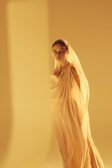 Muse. Beautiful young woman in flowing light fabric with face covered with golden accessories...