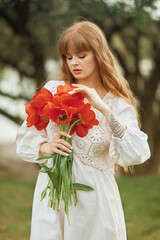 Red-haired girl in a white dress  with a bouquet of red tulips in nature. Grain effect used. 