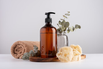 Brown transparent dispenser bottle, cotton towel, loofah sponge and eucalyptus.