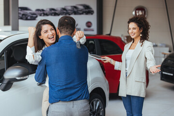 Happy couple hugging after buying a car at the dealership. Excited couple celebrating after buying...