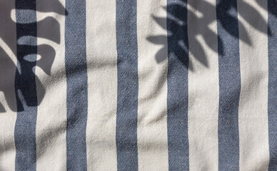 Tropical plants leaves shadows on the blue striped beach towel background