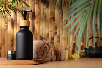 A black pump bottle of lotion or shower gel, sits on a wooden tray against bamboo wall