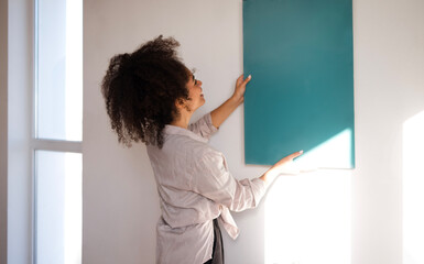A young beautiful mixed-race girl in casual clothes applies a painted sample to the wall. A cute...