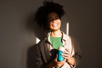 An attractive young girl of mixed race holds a cup of coffee and smiles