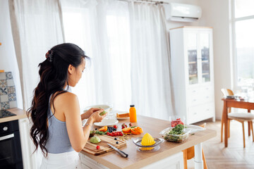 An attractive cute Asian woman smiles and cooks breakfast