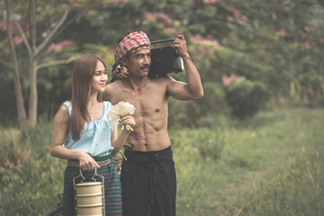 An Asian couple is happily walking on the green rice field rice field. A beautiful wearing a farmer's outfit and a water buffalo background in a rice field in Thailand.