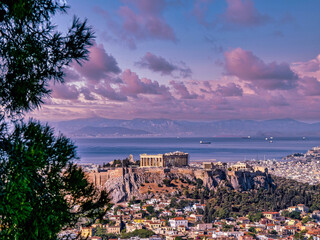 Panoramic view of Athens with Parthenon on the Acropolis and the Saronic sea in the background under a purple cloudy sky. Travel to Greece.