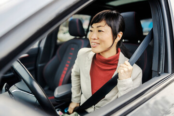 A japanese woman buckling seat belt in her car.