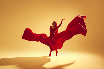 Artistic and deep performance Woman, female dancer in flowing red dress dancing against golden...