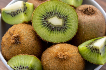 Close-up top view of sliced and whole kiwi fruit in a bowl on the wooden surface
