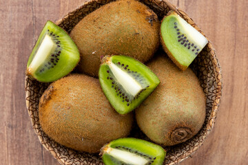 Top view of sliced and whole kiwi fruit in a wicker bowl on the wooden surface