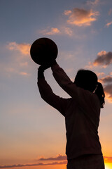 silhouette of a teenage girl holding a basketball ball in her hands at sundown