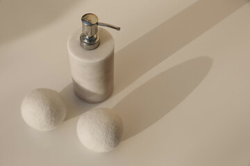 Dryer wool balls and white luxury marble stone soap dispenser bottle on blurred beige table background in sunlight. Long soft shadows. Hygiene, bodycare laundry or bathroom concept. High angle view - Powered by Adobe