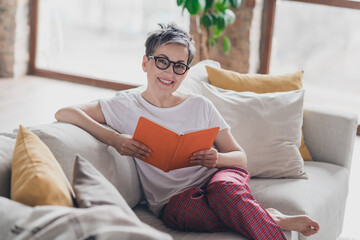Photo of lovely mature lady reading book dressed white garment modern living room rest enjoy...
