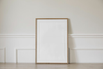 Minimal empty vertical wooden picture frame mockup. White wall with elegant stucco decor. Portrait...
