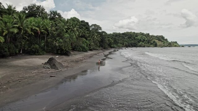 Blonde woman walking along a wild tropical beach alone