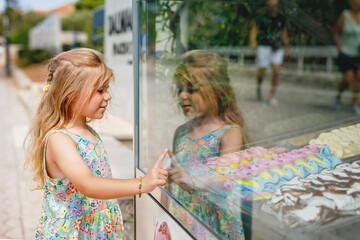 Happy preschool girl choosing and buying ice cream in outdoor stand cafe. Cute child looking at...