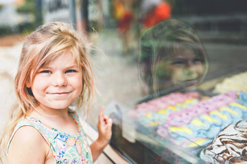 Happy preschool girl choosing and buying ice cream in outdoor stand cafe. Cute child looking at...