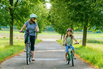 Obraz premium Happy family is riding bikes outdoors and smiling. Mother and daughter, cute little preeschool girl on bicycles, active leisure and sports together.
