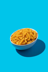 Uncooked fusilli pasta spirals in a white bowl on a blue background