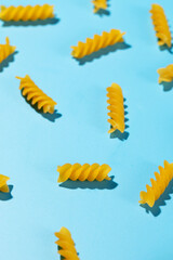 Uncooked fusilli pasta spirals scattered on a blue background in a decorative pattern