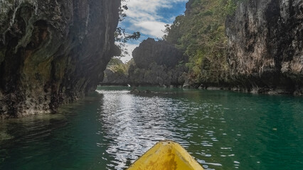 The canoe sails through a picturesque emerald tropical lagoon surrounded by sheer karst cliffs....