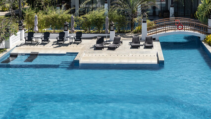 A relaxation area by the blue swimming pool. Sun loungers, tables, sun umbrellas on the terrace.A...