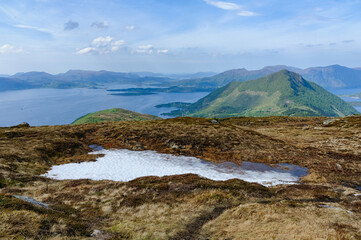 A tranquil highland panorama with a small fjord reflecting the sky as mountains and waterways stretch into the distance.