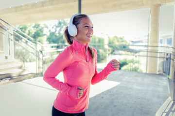 Woman, runner and headphones in city for fitness in sunset, music playlist workout sports. Female...