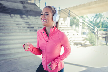 Woman, runner and headphones in city for fitness in sunset, music playlist workout sports. Female person, listen track and training thinking on street for cardio audio, exercise or streaming