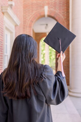 A woman college graduate holding up her black cap in celebration. 