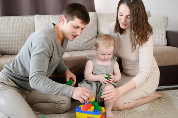 Enthusiastic little girl plays on floor with colorful cubes, tries to build tower together with mom...