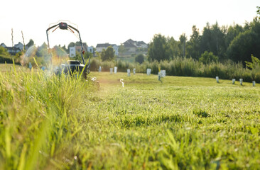 Lawn mower on green grass background in the garden. Low angle of view. Machine for cutting lawns. Cutting of meadow plants. Summer gardening. Banner with copy space