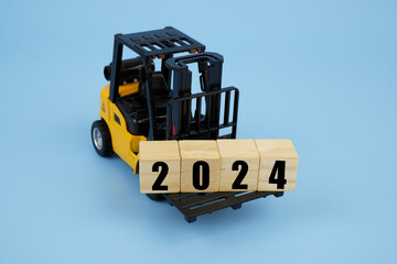 Forklift truck carrying wooden cubes with numbers 2024 on blue background