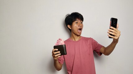 shocked young asian man holding and looking at money wallet and smartphone