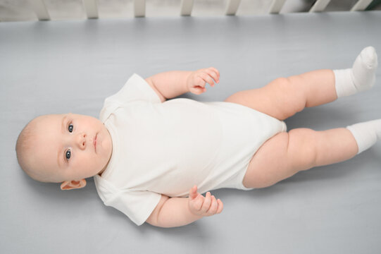 Newborn baby lies in crib and sucks pacifier, top view. Infant wakes up in morning ,stays awake in crib, looking at everything around. Concept of infancy, childhood, products for children, child care.