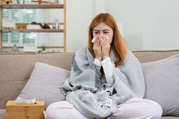 young woman sitting on sofa covered with blanket freezing blowing running nose got fever caught...
