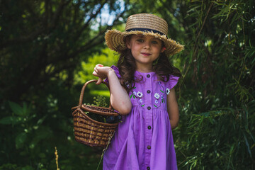 a little girl in a purple dress, with wavy hair and two ponytails in a straw hat against a...