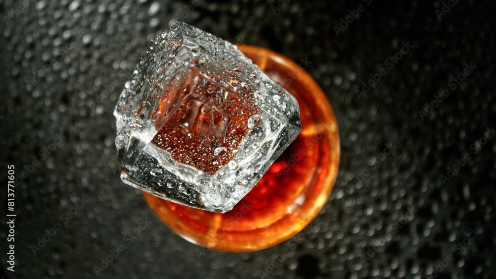 Poster closeup of ice cube falling into glass of whiskey.