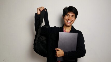 college young asian man happy while carrying bag and holding laptop