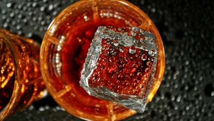 Closeup of ice cube falling into glass of whiskey.