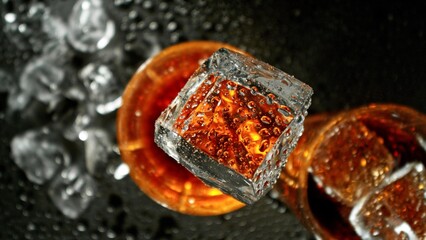 Closeup of ice cube falling into glass of whiskey.
